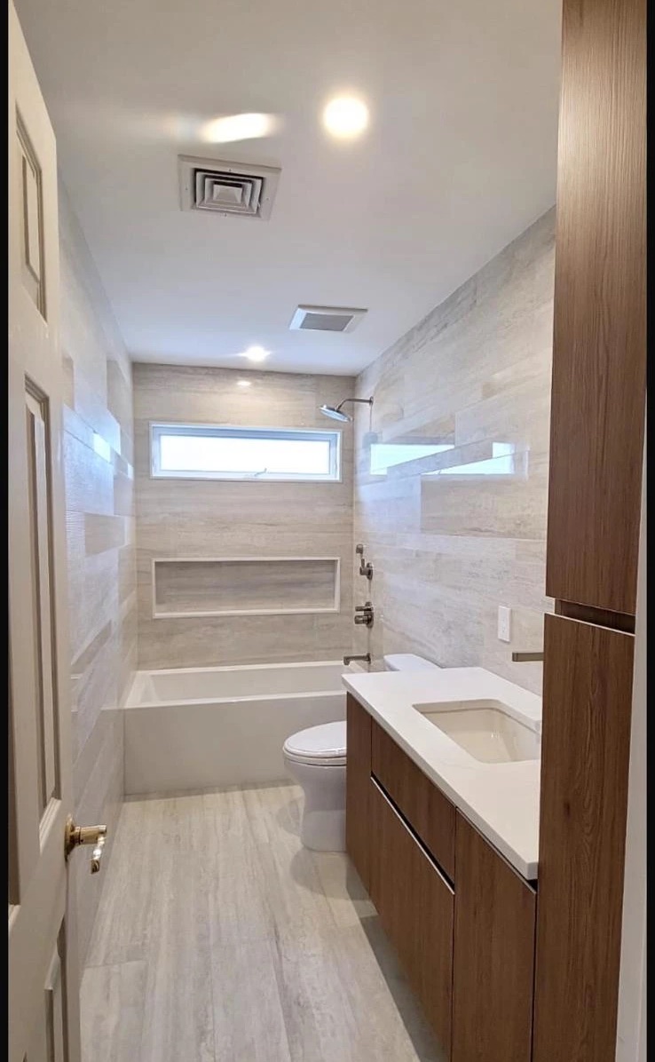Finished bathroom with tiled walls and floor, tub, vanity and new lighting